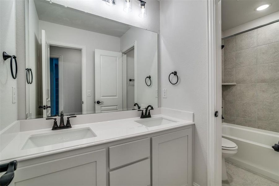 Full main floor bathroom with dual sinks, tile patterned floors, vanity, toilet, and tiled shower / bath