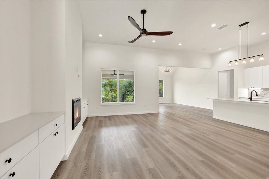 Unfurnished living room featuring a glass covered fireplace, a ceiling fan, light wood-style flooring, recessed lighting, and a chandelier