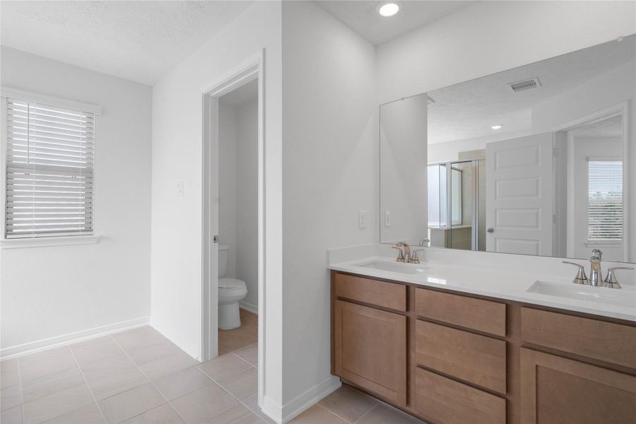 The primary bathroom is move-in ready! It showcases stained cabinetry paired with light countertops, dual vanity sinks, a large mirror, a spacious walk-in closet with built-in shelving, toilet compartment, high ceilings, custom paint, and stylish modern finishes throughout.