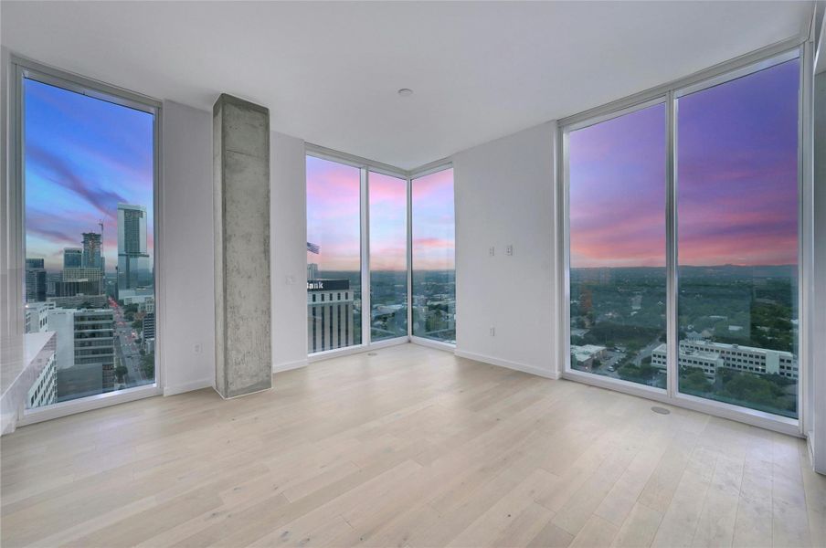Stunning Corner Living Room with Panoramic City Views. This modern corner living room offers breathtaking panoramic views of the Austin skyline through floor-to-ceiling windows. The spacious, open layout is bathed in natural light, creating a bright and airy atmosphere perfect for both relaxation and entertaining. The light wood flooring adds warmth to the contemporary design, while the exposed concrete pillar adds a touch of urban sophistication. Watch the sunset over the city and enjoy the vibrant colors of the sky from the comfort of your own home. Stunning Corner Living Room with Panoramic City Views. This modern corner living room offers breathtaking panoramic views of the Austin skyline through floor-to-ceiling windows. The spacious, open layout is bathed in natural light, creating a bright and airy atmosphere perfect for both relaxation and entertaining. The light wood flooring adds warmth to the contemporary design, while the exposed concrete pillar adds a touch of urban sophistication. Watch the sunset over the city and enjoy the vibrant colors of the sky from the comfort of your own home.