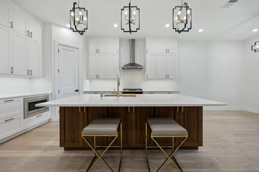 Kitchen with stainless steel microwave, a kitchen island with sink, light wood-type flooring, and wall chimney range hood