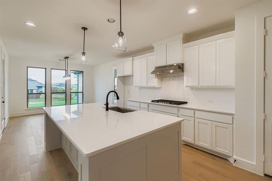 Kitchen with light wood-type flooring, white cabinets, decorative light fixtures, a center island with sink, and recessed lighting Kitchen with light wood-type flooring, white cabinets, decorative light fixtures, a center island with sink, and recessed lighting