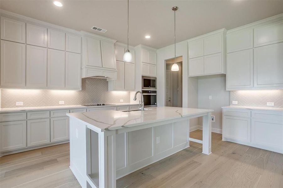 Kitchen with light hardwood / wood-style floors, backsplash, stainless steel appliances, and an island with sink