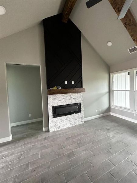 Unfurnished living room featuring baseboards, visible vents, wood finish floors, vaulted ceiling with beams, and a stone fireplace