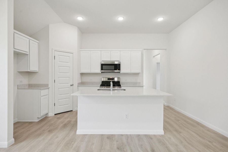 Kitchen featuring an island with sink, appliances with stainless steel finishes, light countertops, light wood finished floors, and white cabinets