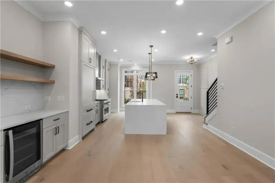 Open-concept kitchen with light wood-finish flooring, white cabinetry, a central island with a sink, stainless steel appliances, and a built-in beverage refrigerator