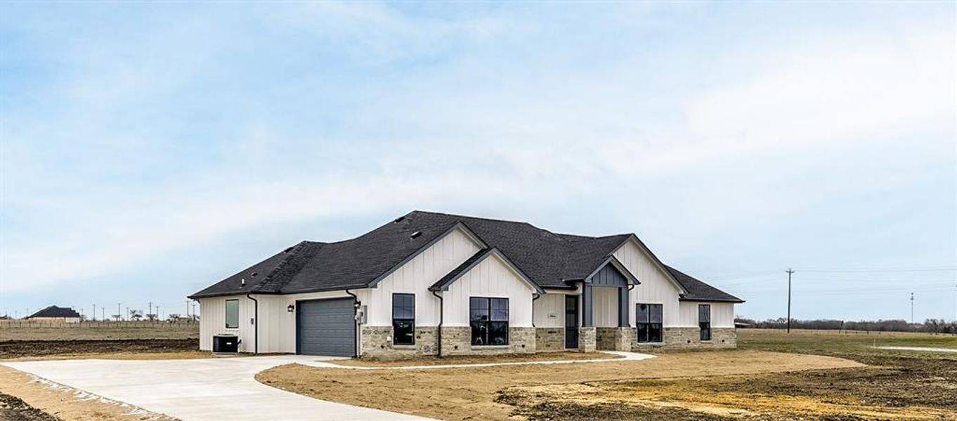 Modern inspired farmhouse featuring driveway, stone siding, a shingled roof, and board and batten siding