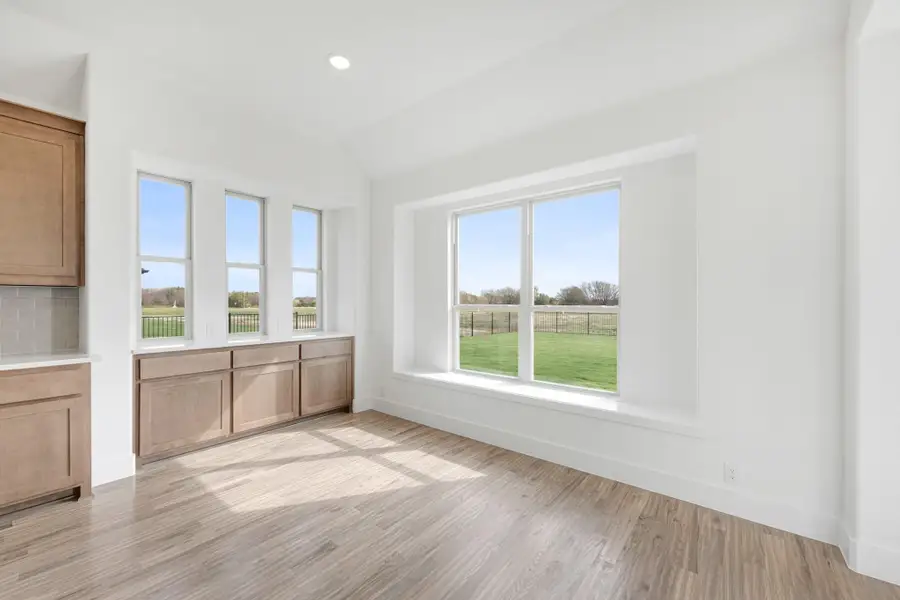 Bright dining area with light wood floors, large windows, and wood cabinetry overlooking a green yard Bright dining area with light wood floors, large windows, and wood cabinetry overlooking a green yard