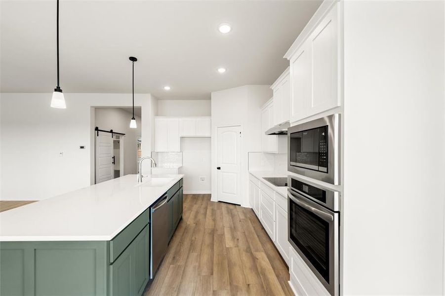 Dual tone kitchen featuring two tone color scheme, a barn door, stainless steel appliances, a kitchen island with sink, and light wood-style floors