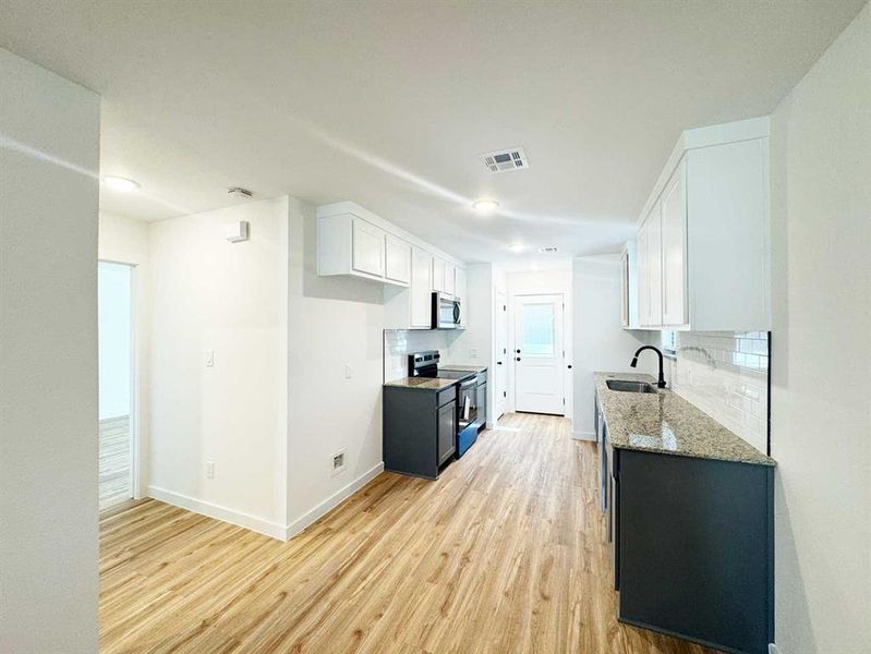 Kitchen with appliances with stainless steel finishes, light stone countertops, a sink, and light wood-style floors