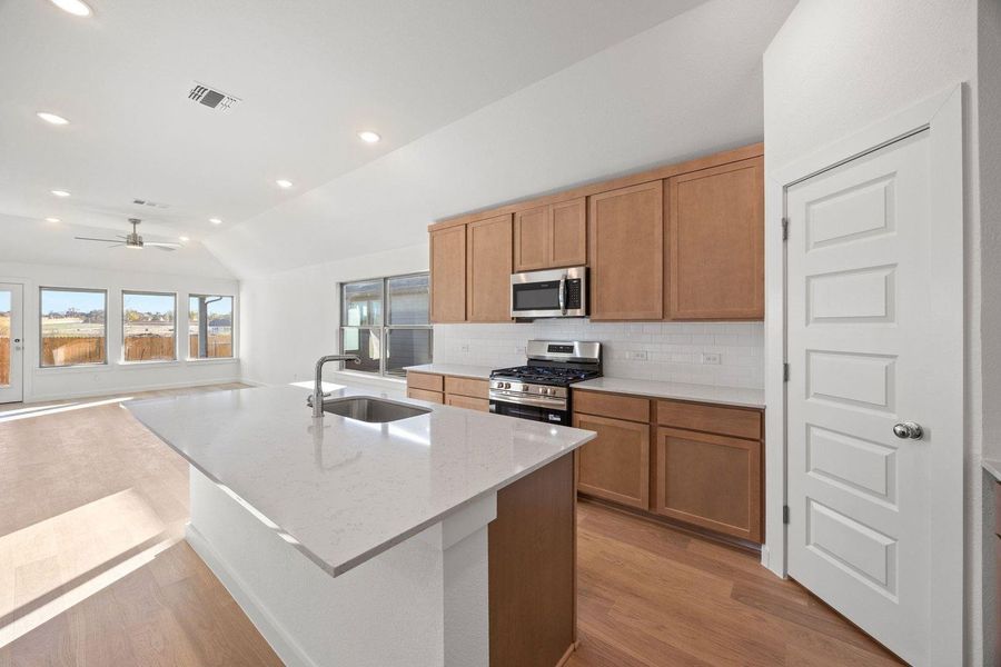 A well-lit kitchen with a spacious island flows into a living area with large windows, offering an inviting open concept.