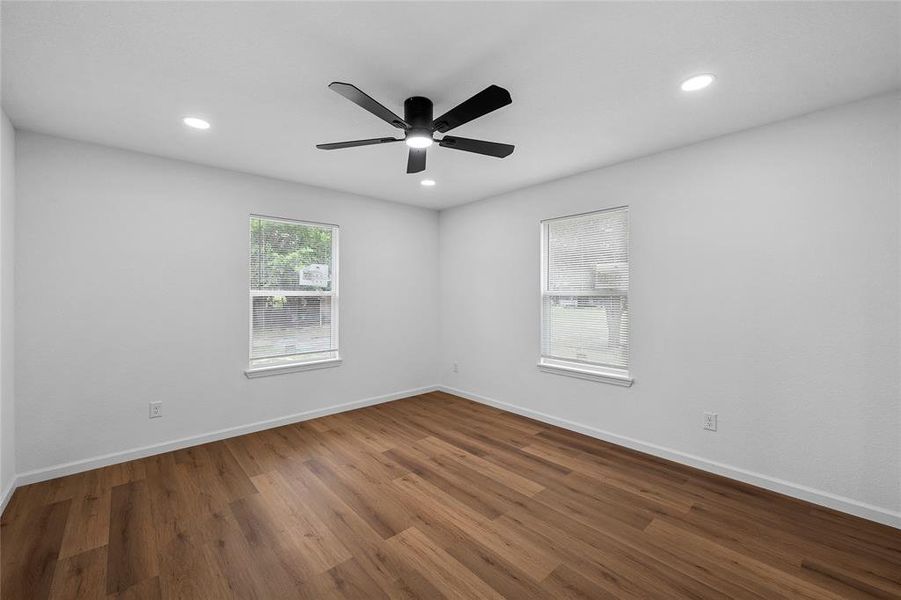 Room featuring wood-finish flooring, two windows, recessed lighting, and a ceiling fan with integrated lighting Room featuring wood-finish flooring, two windows, recessed lighting, and a ceiling fan with integrated lighting