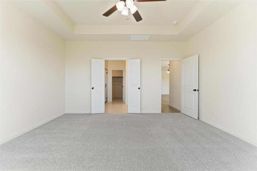 Unfurnished bedroom with carpet, a tray ceiling, a spacious closet, and ceiling fan