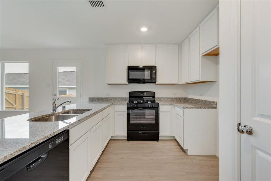 Kitchen with white cabinets, light hardwood / wood-style floors, sink, and black appliances