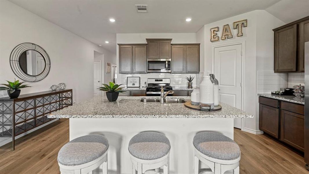 Kitchen featuring light stone countertops, a kitchen island with sink, dark brown cabinets, appliances with stainless steel finishes, and recessed lighting