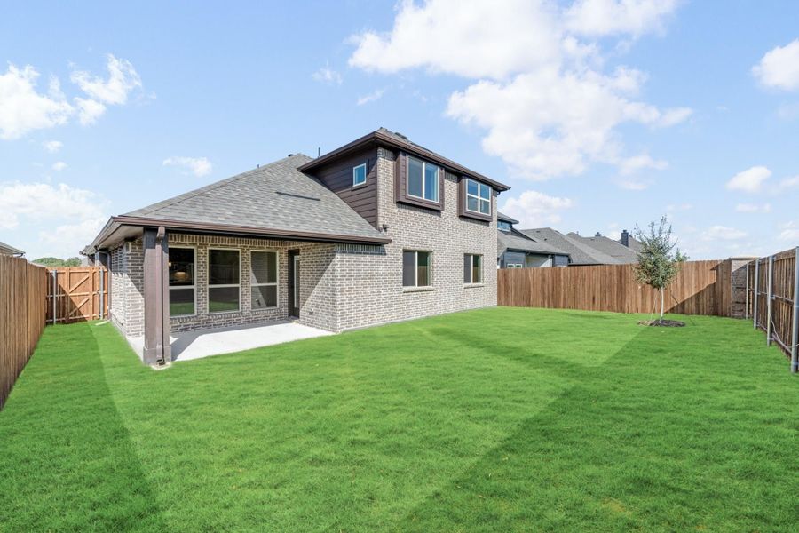 Two-story brick home with covered patio, large fenced backyard, and green lawn