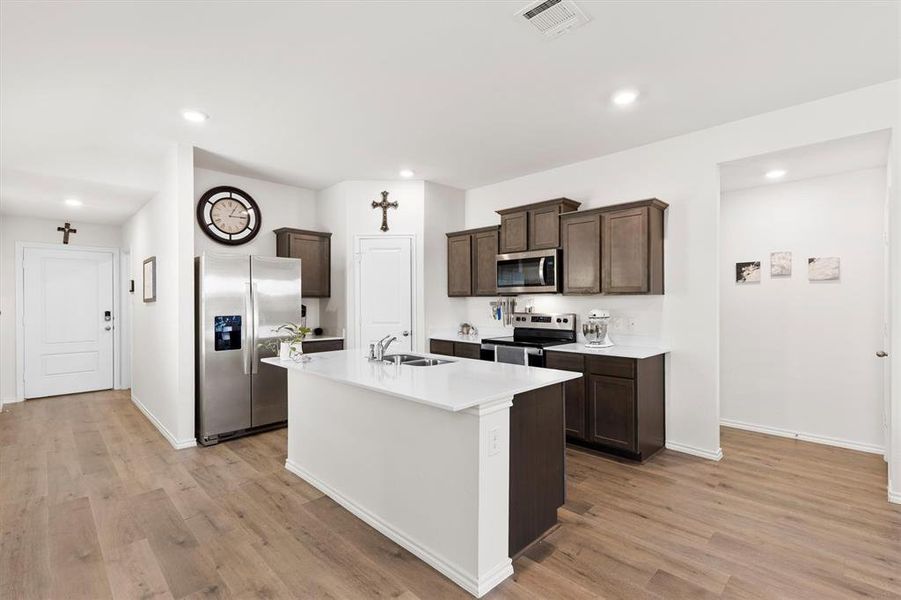 Kitchen with stainless steel appliances, dark wood finish cabinetry, a center island with sink, light wood-type flooring, and recessed lighting Kitchen with stainless steel appliances, dark wood finish cabinetry, a center island with sink, light wood-type flooring, and recessed lighting
