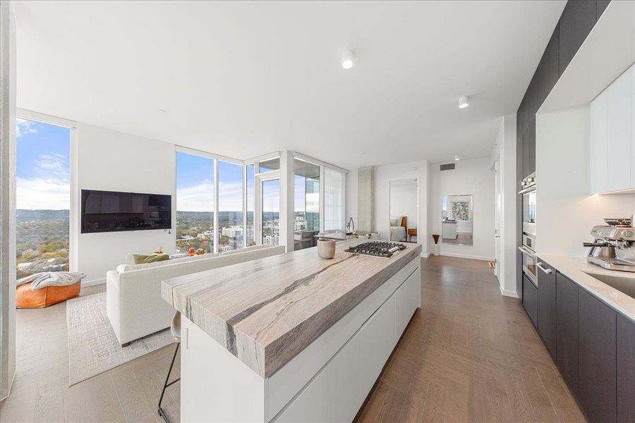 A designer kitchen anchored by upgraded Fantasy Ocean marble countertops and custom cabinetry, connecting directly to a light-filled living space with sweeping skyline vistas.