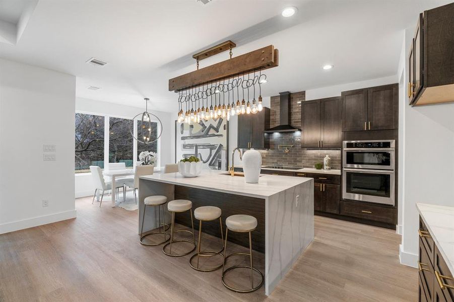 Kitchen with a center island with sink, light wood-type flooring, backsplash, wall chimney exhaust hood, and stainless steel double oven