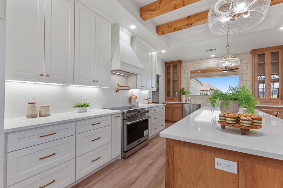 Kitchen featuring beamed ceiling, stainless steel appliances, light stone counters, decorative light fixtures, and dual tone cabinets Kitchen featuring beamed ceiling, stainless steel appliances, light stone counters, decorative light fixtures, and dual tone cabinets