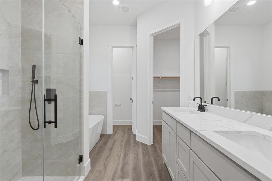 Modern bathroom featuring a dual vanity with a quartz countertop, frameless glass shower enclosure, freestanding soaking tub, wood-finish flooring, and matte black fixtures