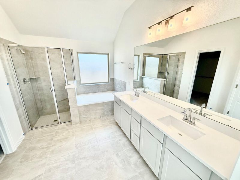 Full bathroom featuring a garden tub, a shower stall, double vanity, lofted ceiling, and light tile patterned floors