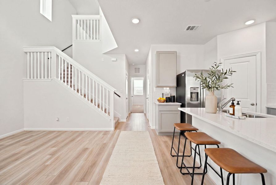 Gleaming light wood flooring extends through the open entry level next to a modern kitchen.