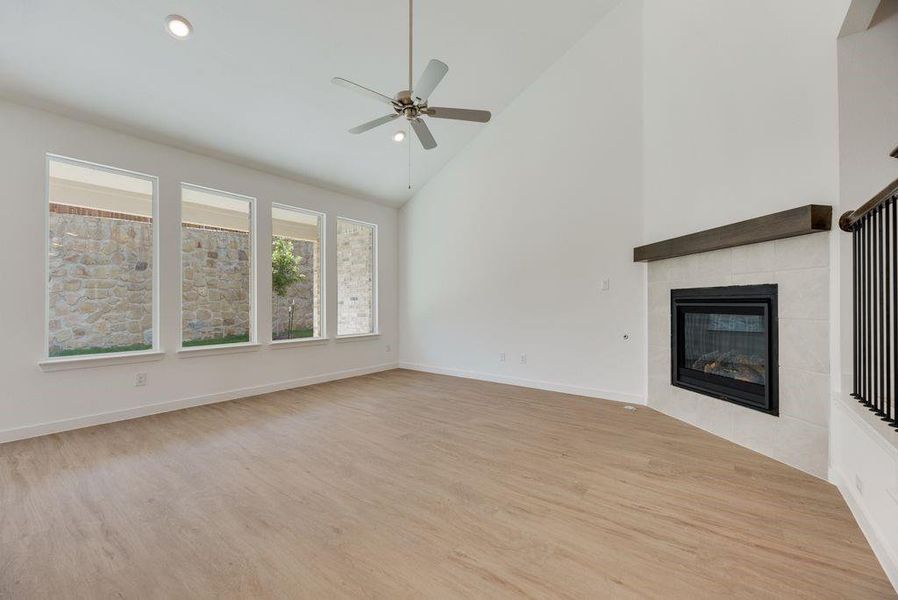Unfurnished living room with high vaulted ceiling, wood finished floors, a tile fireplace, ceiling fan, and recessed lighting