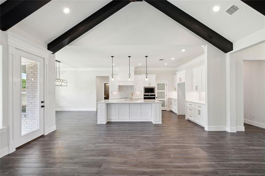 Kitchen with lofted ceiling with beams, tasteful backsplash, decorative light fixtures, an island with sink, and built in microwave