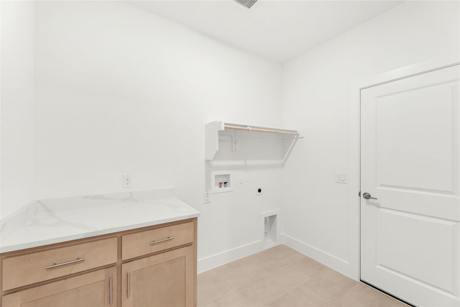 Laundry room with wood cabinets, quartz countertop, wall shelf, and washer and dryer hookups on tile floor