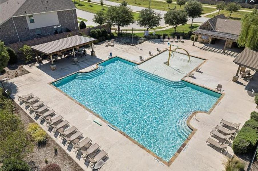 Resort-style community pool area featuring a large swimming pool with gradual entry steps, an integrated splash pad, and a shaded outdoor lounge area
