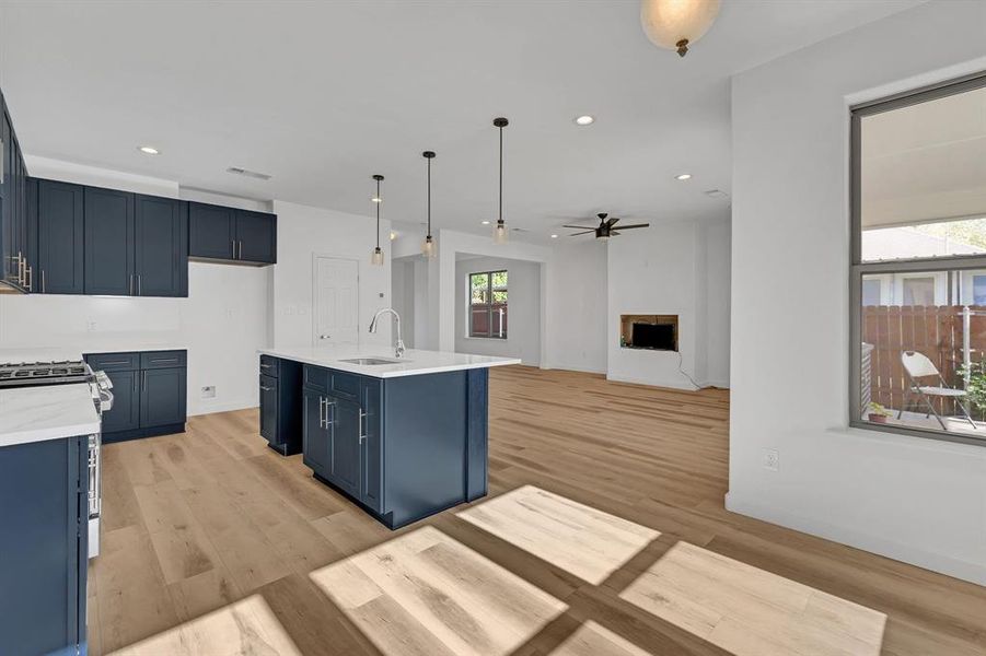 Kitchen featuring an island with sink, blue cabinets, a fireplace, recessed lighting, and pendant lighting