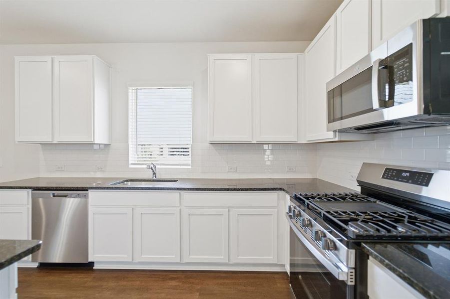 Bright kitchen featuring white shaker cabinetry, dark countertops, a stainless steel gas range, and a subway tile backsplash