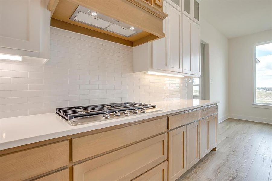 Kitchen featuring light wood-type flooring, backsplash, light brown cabinetry, stainless steel gas stovetop, and premium range hood