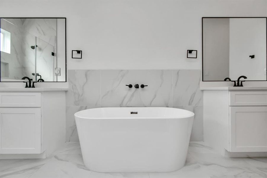 Indulge in relaxation with a spacious primary bath boasting a luxurious bathtub and double sinks with vanity and a large glass frame standing shower.