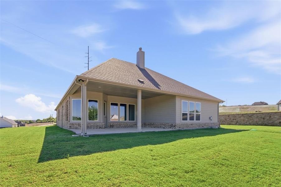 Back of house featuring a yard, a patio area, brick siding, and roof with shingles