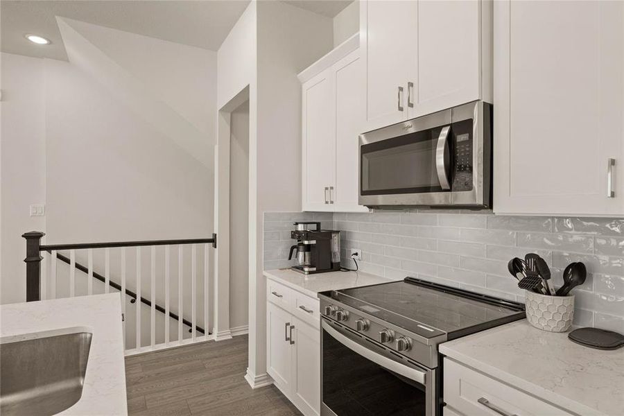 Kitchen featuring light stone counters, stainless steel appliances, backsplash, and white cabinets