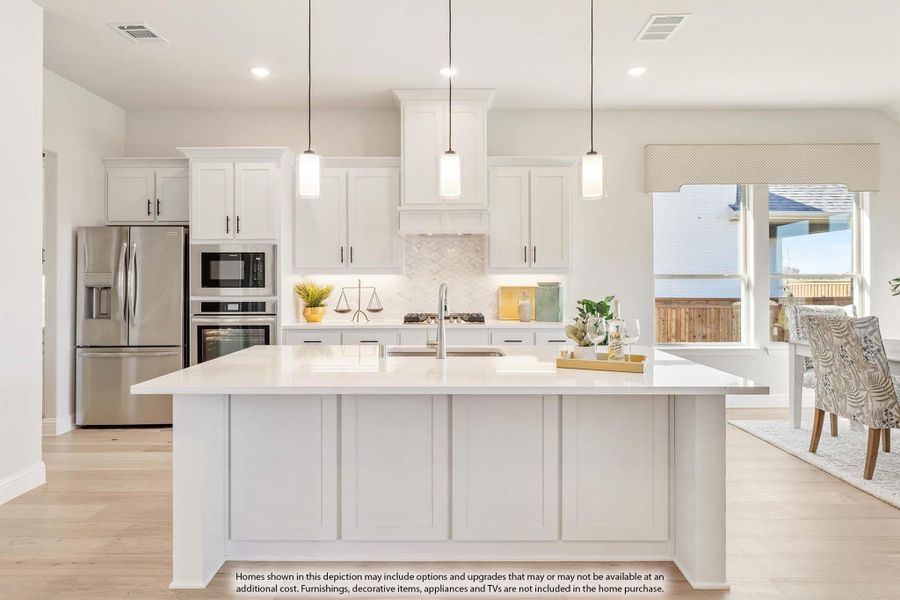 White kitchen with large center island, pendant lights, stainless steel appliances, and light hardwood floors
