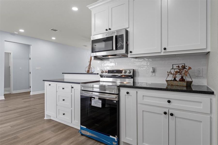 Kitchen featuring stainless steel appliances, white cabinets, decorative backsplash, recessed lighting, and light wood finished floors