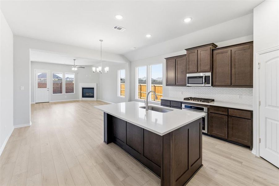 Kitchen featuring dark brown cabinetry, a glass covered fireplace, a kitchen island with sink, light wood-type flooring, and recessed lighting
