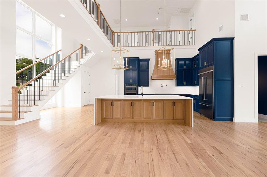 Kitchen featuring hanging lights, a spacious island, stainless steel appliances, blue cabinetry, and light wood-style floors