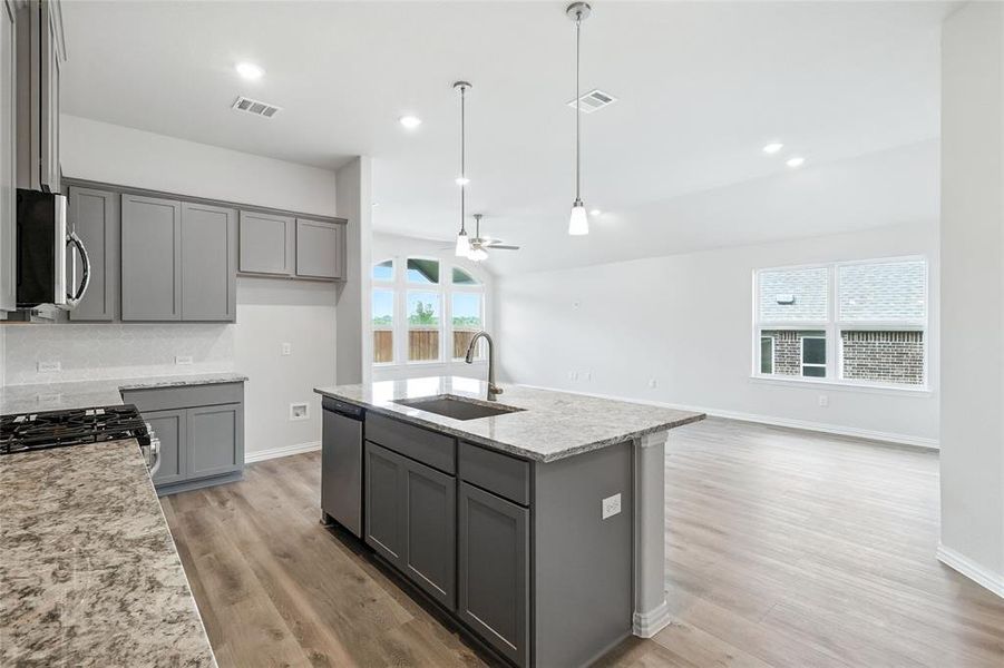 Kitchen featuring gray cabinetry, an island with sink, light stone countertops, a ceiling fan, and open floor plan