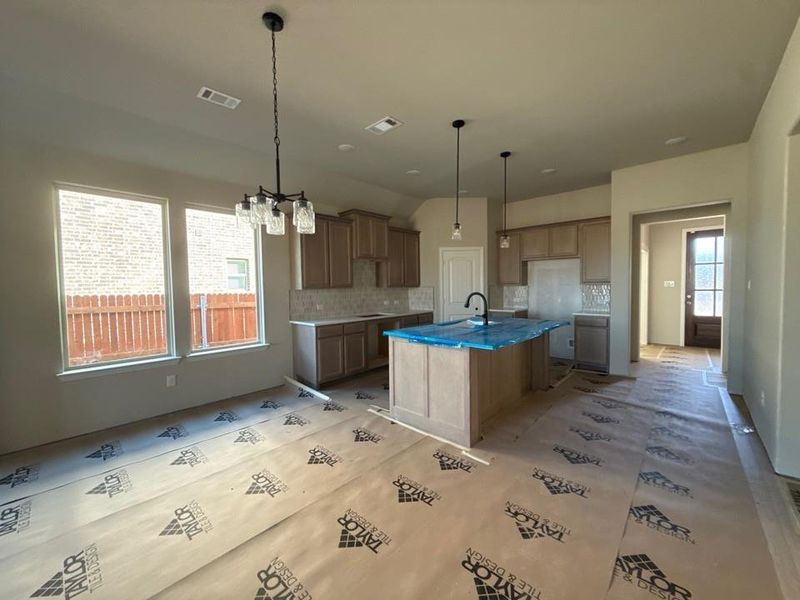 Kitchen with a center island with sink, backsplash, a kitchen breakfast bar, and wood finish cabinetry