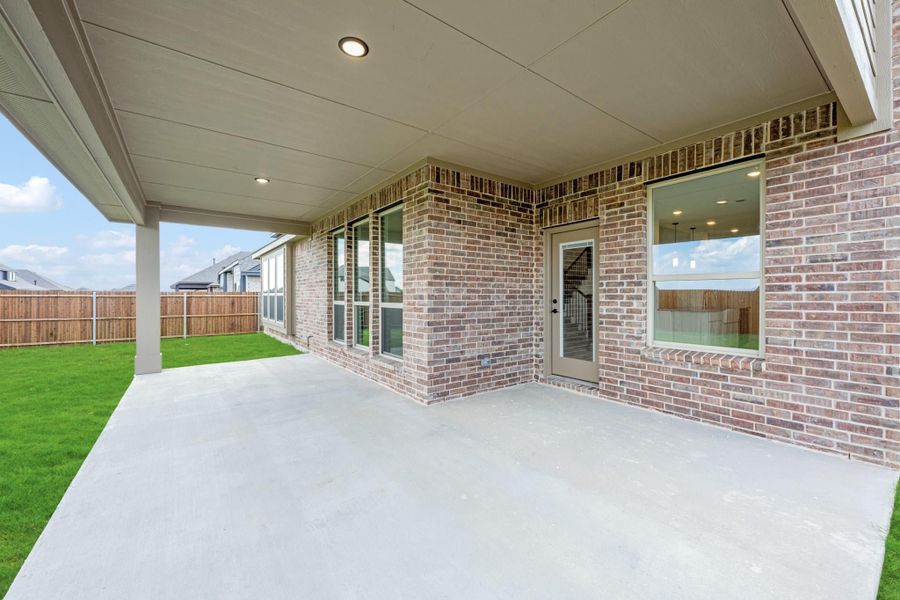 Covered concrete patio with recessed lighting along brick home exterior and fenced backyard with green lawn Covered concrete patio with recessed lighting along brick home exterior and fenced backyard with green lawn