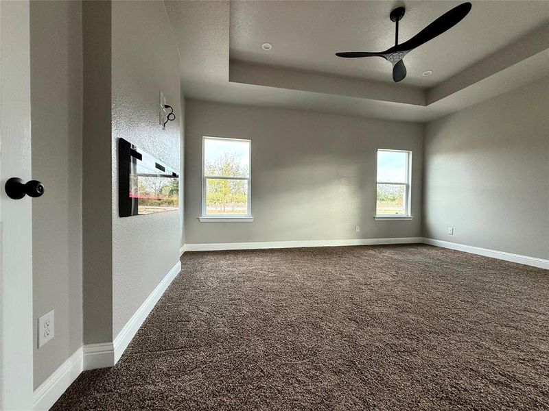 MASTER room featuring dark colored carpet, a tray ceiling, a textured wall, and ceiling fan  and Electric fire place.
