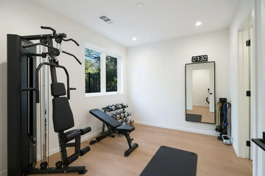 Exercise area with light wood-style floors and recessed lighting