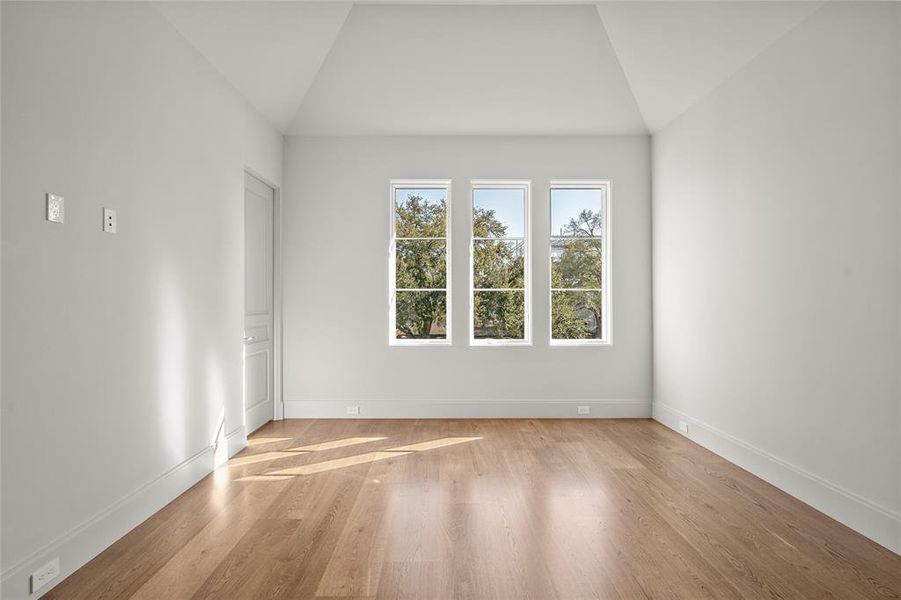 Flooded with natural light, this secondary bedroom offers a serene retreat with large windows framing lush treetop views. The vaulted ceiling enhances the sense of space, while white oak hardwood floors add warmth and sophistication. A private ensuite bath and walk-in closet provide both comfort and functionality, making this a perfect space for relaxation.