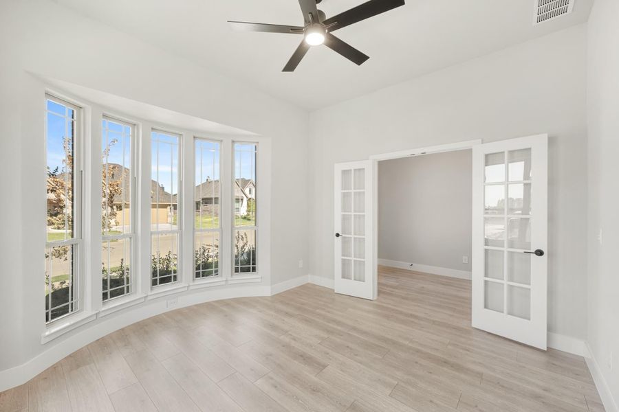 Empty room with bay windows, French doors, ceiling fan, and light hardwood floors Empty room with bay windows, French doors, ceiling fan, and light hardwood floors