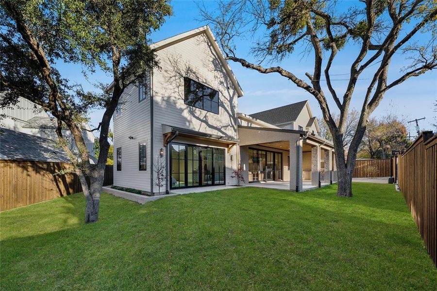 Expansive backyard featuring a manicured lawn, mature trees, and a spacious covered patio