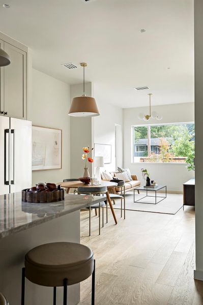 Kitchen featuring light wood-style floors, decorative light fixtures, freestanding refrigerator, dark stone counters, and open floor plan